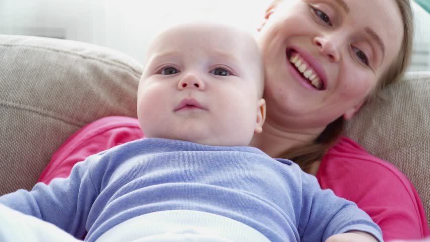 Young mother playing with her 6 months son's legs laying on sofa closeup