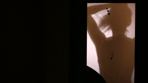 Silhouette of a woman, behind a glass door. She gathers her hair in the tail