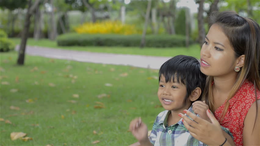 Young Asian mother and her son, sitting in a park, talking and spending time