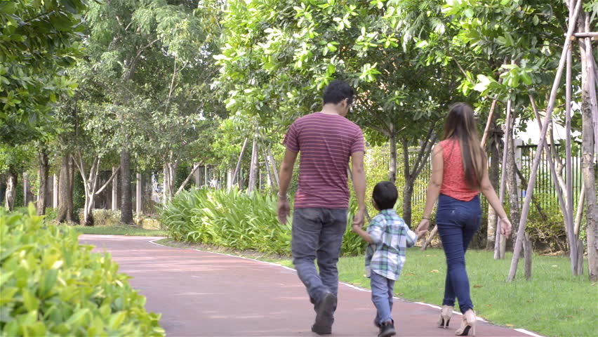 Happy young Asian family walking together in a park - dolly tracking shot.