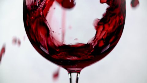 Filling wine glass with red wine super slow motion macro shot on white background.