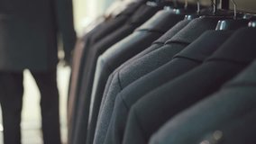 Elegant young man in suit choosing jacket in clothing store