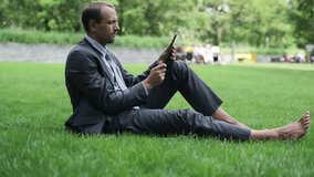 Businessman with documents chatting tablet computer in the park
