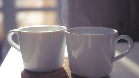 Two beautiful white cups stand on a stoop in the rays of the sun, slow pairs are spinning in the light. slowmotion. 1920x1080