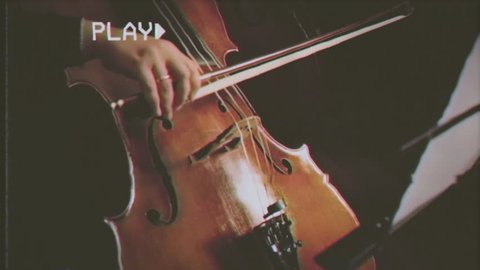 Fake VHS tape: close up of a musician playing a cello in an orchestra.
