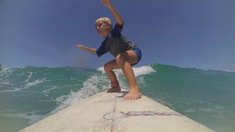 Child learning surfing with young father in tropicals. Cute boy on surfboard on ocean wave. Enjoying summer vacation in surf camp. POV
