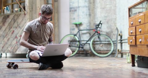 Young adult male sitting on skateboard using laptop