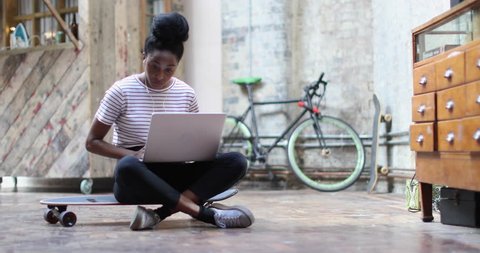Young adult female sitting on skateboard using laptop