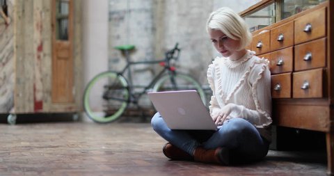 Young adult female sitting on floor working on laptop