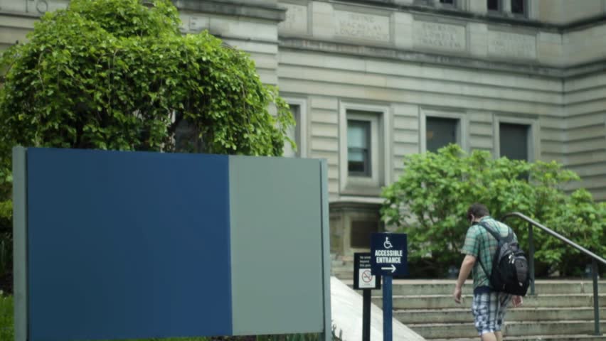 People walk by generic blank sign up to concrete building on rainy day