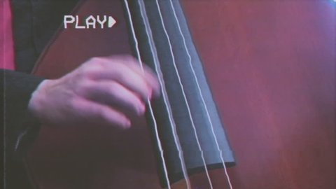 Fake VHS tape: close up of a musician playing a double bass, fingers picking the strings.
