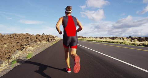 Triathlon - Triathlete man running in triathlon suit training for ironman race. Male runner exercising on Big Island Hawaii. SLOW MOTION TRACKING RED EPIC.