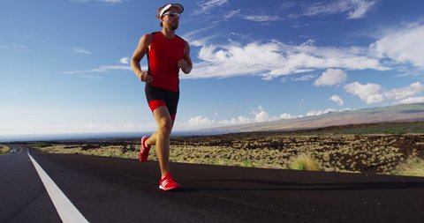 Triathlon - Triathlete man running in triathlon suit training for ironman race. Male runner exercising in beautiful landscape on road on Big Island Hawaii. RED EPIC SLOW MOTION.