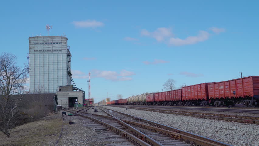 A train railtracks on the side of the construction factory with a big cylinder inside the factory