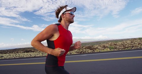 Runner man running in triathlon suit training for Iron man on Hawaii. Fit male triathlete exercising on road. SLOW MOTION RED EPIC.