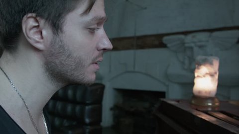 A young man with an easy shield plays the piano and sings. A handsome man with a chain on his neck sings on the front of the fireplace. Lamp on the piano. The camera is enlarged on the lips.