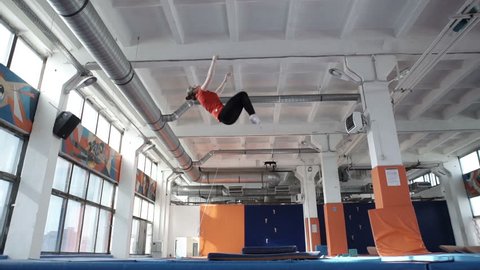 Young athetic girl is doing exercise in slow motion on a trampoline indoors