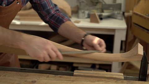 Cabinet maker polishes the cabriolet leg with a file. He works in a small family joiner’s shop/Cabinetmaker Polishes Cabrioli Leg in his Workshop