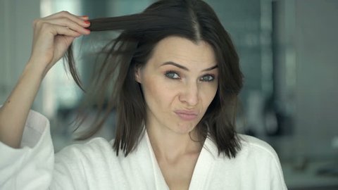 Unhappy woman on bathrobe checking her hair in mirror in bathroom 

