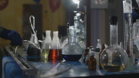 The scientist and his assistant conduct chemical experiments in an underground laboratory. Chemical laboratory. Close-up of the flasks with the chemicals that stand on the table, boil and smoke.