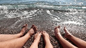 Closeup of barefoot family sitting together at seashore admiring sea view. Dad, mom and son having fun on beach in summer. Real time full hd video footage.