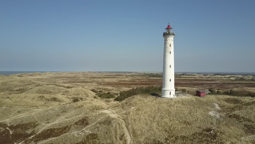 Aerial, flight around Lyngvig lighthouse over grass covered dunes on Denmarks North Sea coast
