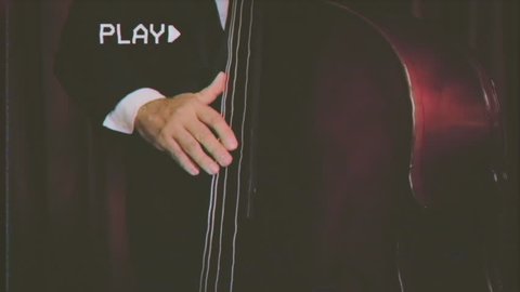 Fake VHS tape: a musician playing a double bass in an orchestra. Middle shot.
