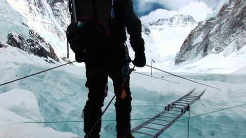 A mountaineer crossing a ladder over a glacier on route to the summit of Mount Everest. Nepalese Himalayas.