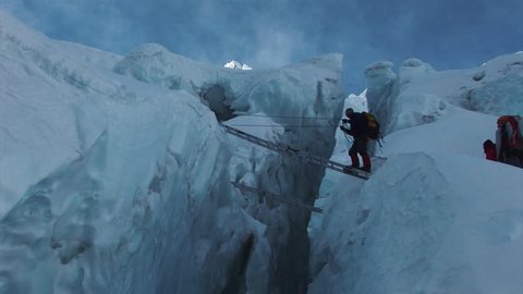 A mountaineer crossing a ladder over a glacier on route to the summit of Mount Everest. Nepalese Himalayas.
