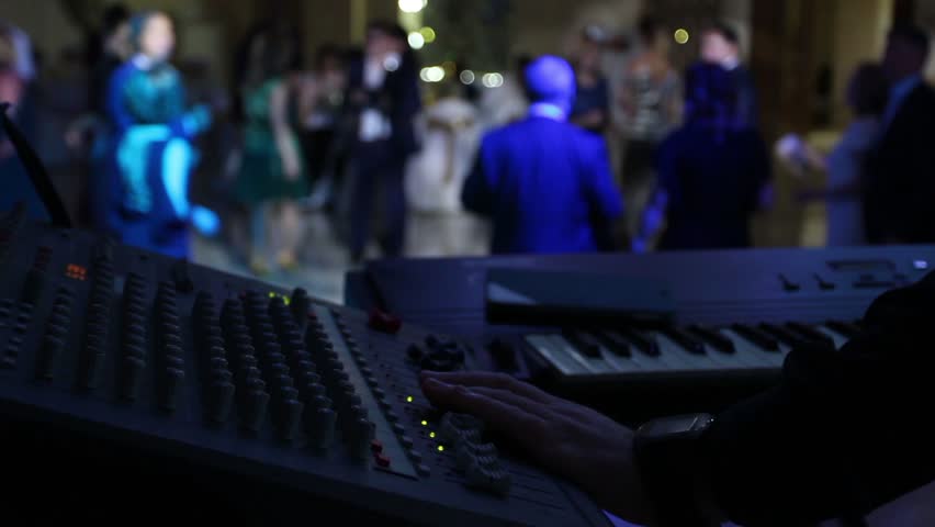 The musician in the foreground adjusts the sound and plays the keyboard instrument. People dance in the background. Royalty-Free Stock Footage #26429903