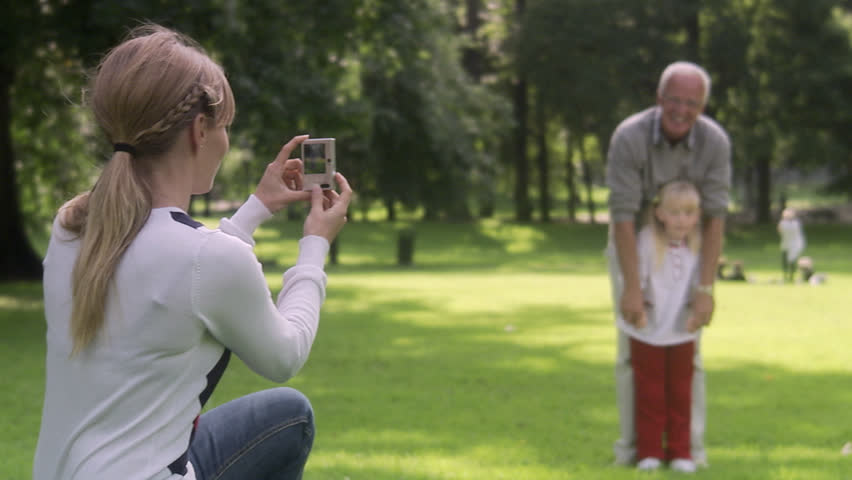 Woman, senior man and girl taking photographs in a park