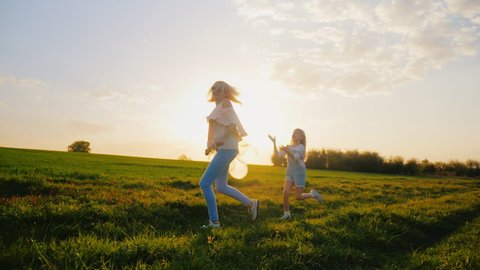 A young woman is playing with her daughter for 6 years. Cheer together, the girl runs after balloons. On a beautiful green meadow . Concept - happy together, active rest, healthy lifestyle
