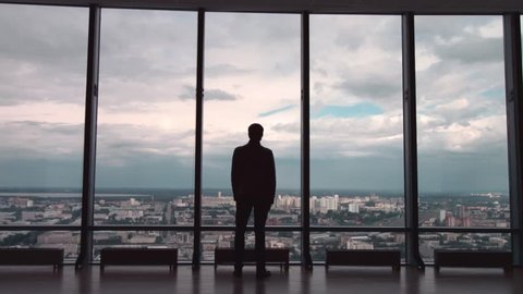 Rear view of man in formal suites who stand in front of panoramic window with city view. a man stands in front of big panoramic wiindow view from back.