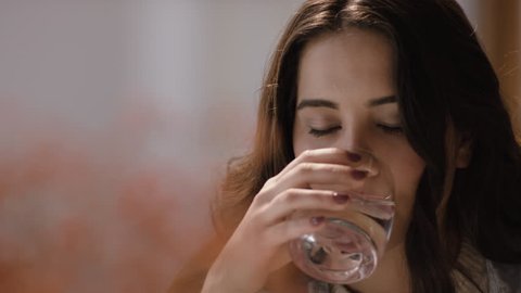 Beautiful brunet young woman drinking a glass of water at home, close up