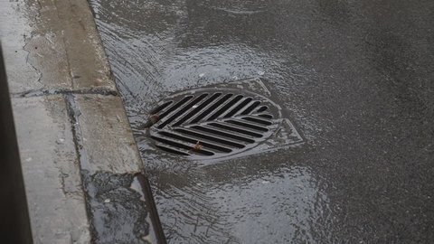 Slow motion water going down a city drain. Toronto, Canada. Wide shot.
