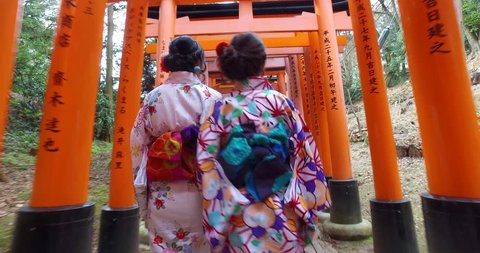 POINT OF VIEW: Women wearing traditional kimono walking inside Fushimi Inari Shrine. A Japanese monument, famous for its thousands of vermilion torii gates. 