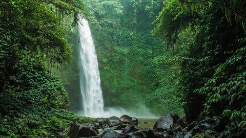 Amazing Nungnung waterfall, Falling water hitting water surface, some huge rocks seeable in front of frame. Lush green leafes is moving from the wind, Bali, Indonesia