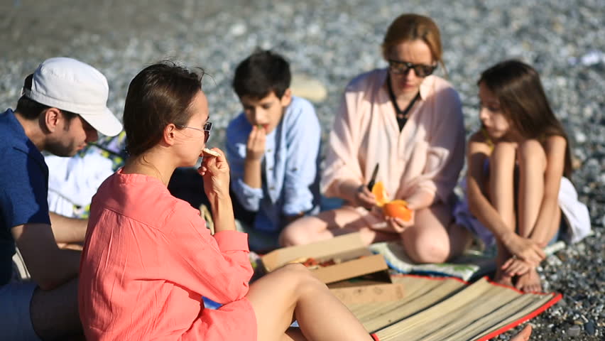 Friends with children eating pizza on the beach. Picnic by the sea on the beach