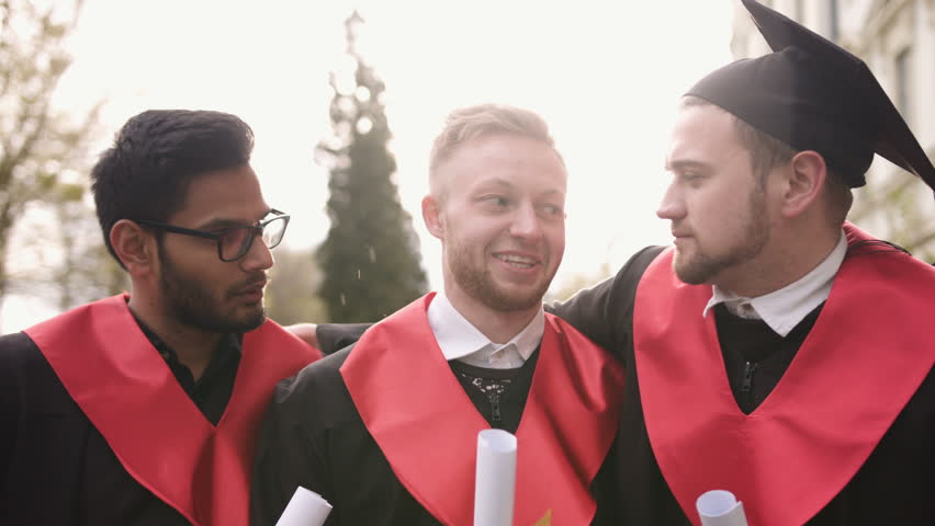 Portrait of three friends graduate looking at the camera smiling in the street sun shines and the snow falls