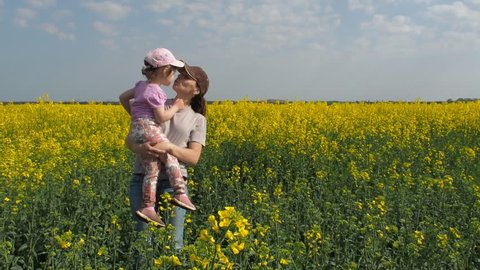 Mother hugging her daughter in nature. Woman with little girl on yellow field. A happy family. Rapeseed field.