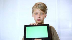 Sad blond kid holding touchpad in hands with broken blank green display still working. Real time full hd video footage.