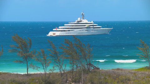 Luxury Yacht Anchored off the Tropical Bahamas Coast in an Exotic Turquoise Blue Water Setting with Waves Breaking onto a Beach during a Sunny Day