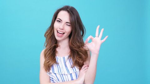 Young cheerful woman winking and showing gesture okay isolated