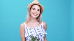 Young cheerful woman wearing hat holding pineapple isolated over blue background