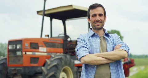 Portrait of a handsome young farmer standing in a shirt and smiling at the camera, on a tractor and nature background. Concept: bio ecology, clean environment, beautiful and healthy people, farmers.
