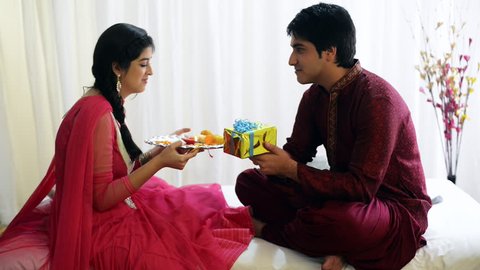 Pan shot of a teenage girl holding a puja thali and her brother sitting with a present in front of her