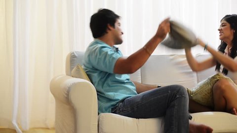 Pan shot of a brother and sister fighting with pillows