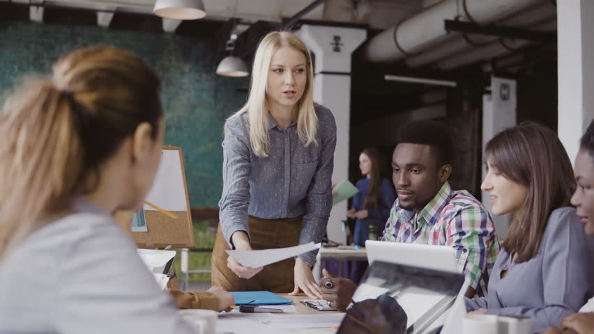 Blonde woman team leader giving direction to mixed race team of young guys. Creative business meeting at modern office. Royalty-Free Stock Footage #26472704