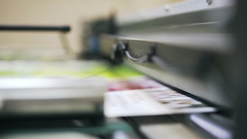 Blurred image of colorful posters being printed at an industrial printer in a printing plant. Locked down slow motion close up shot