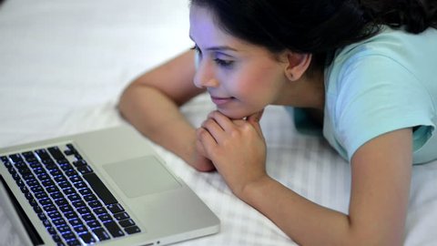 Locked-on shot of a woman lying on the bed and using a laptop